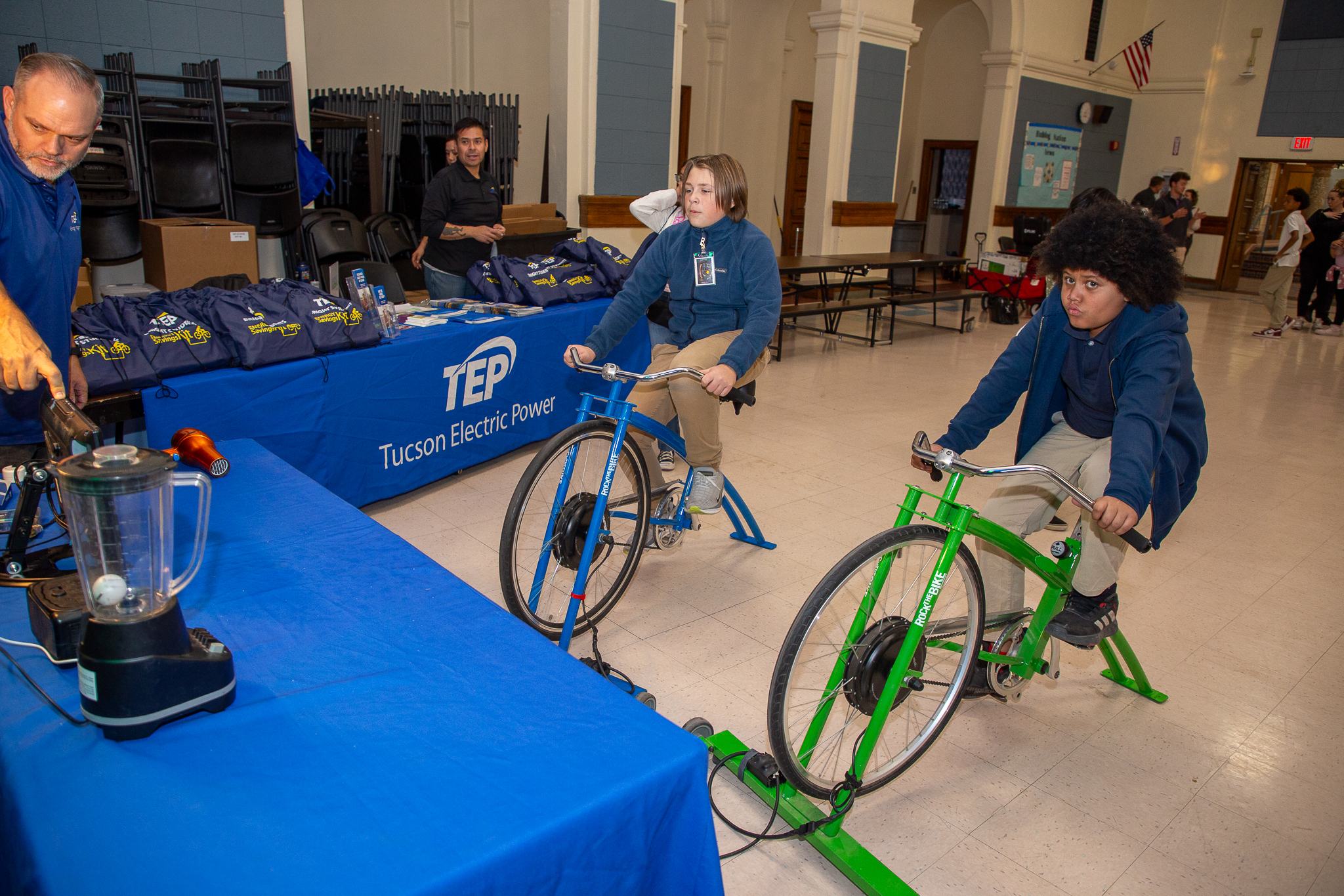 Two boys ride stationary bikes to power kitchen appliances like a blender