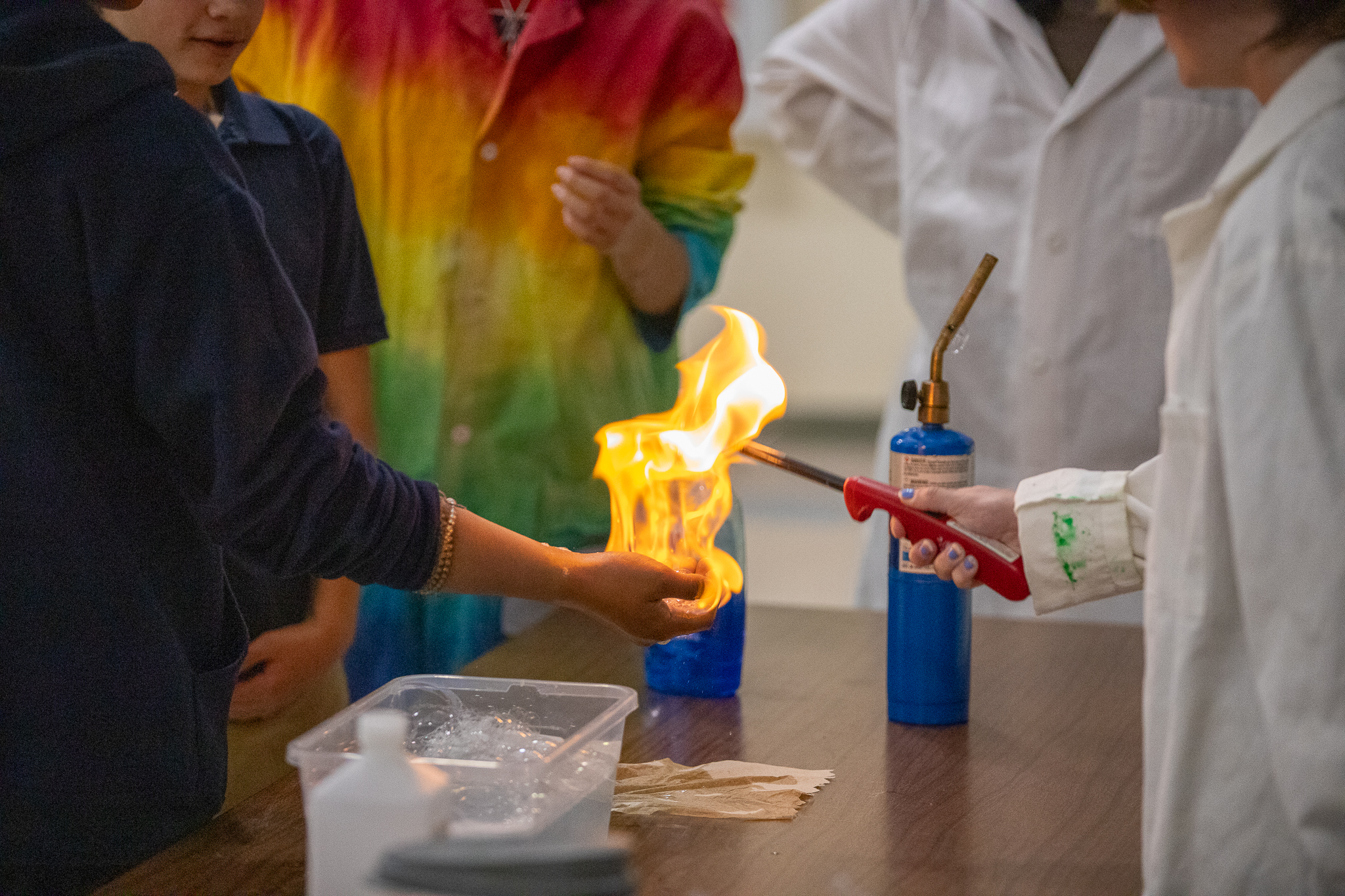 A teacher in a lab coat lights something on fire in a student's hand