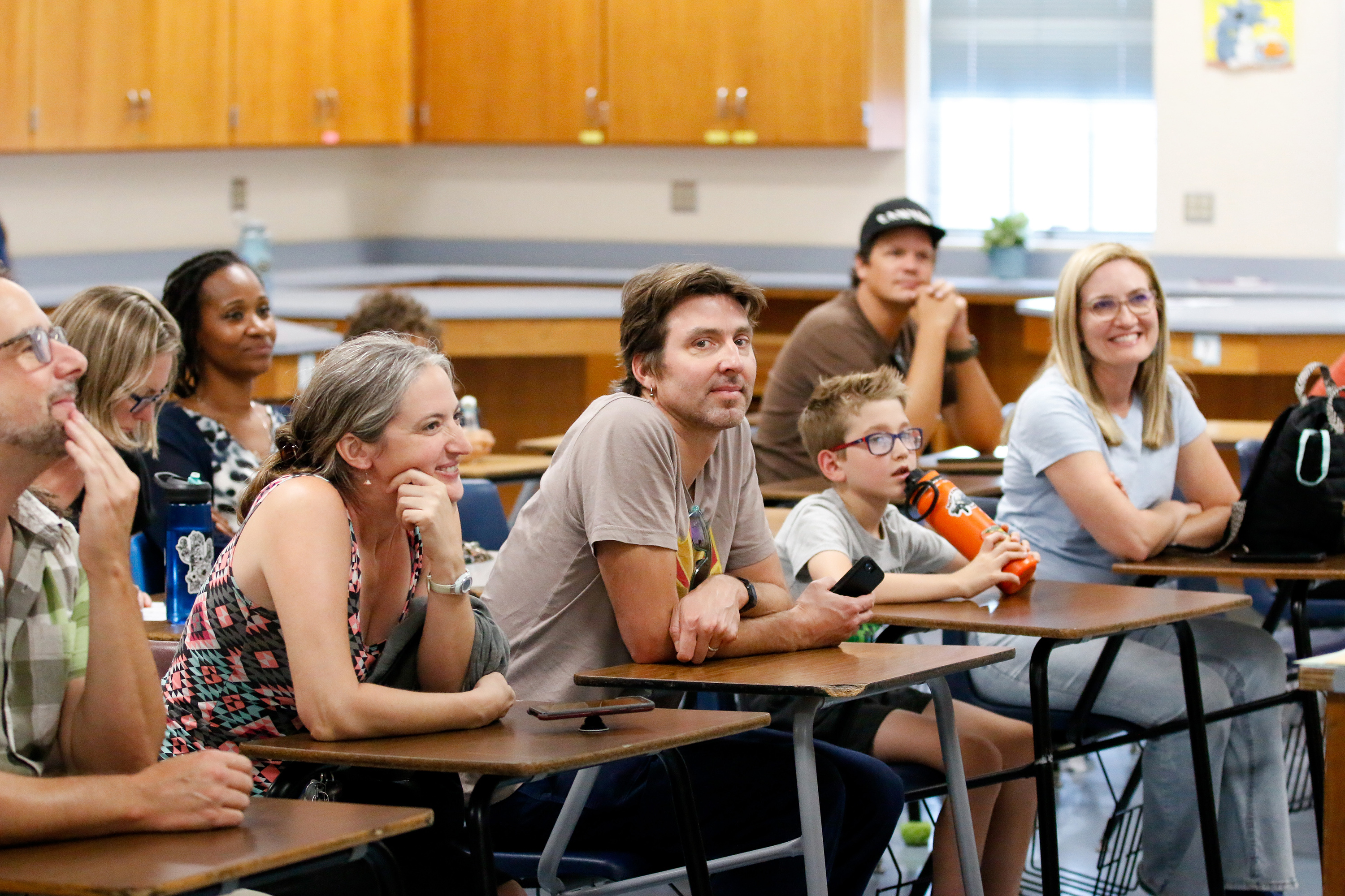 Families sit in desks and listen to the teacher's presentation