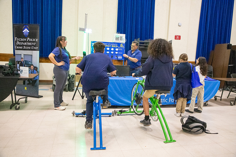 Two preteen boys pedal on bicycles to power up lightbulbs
