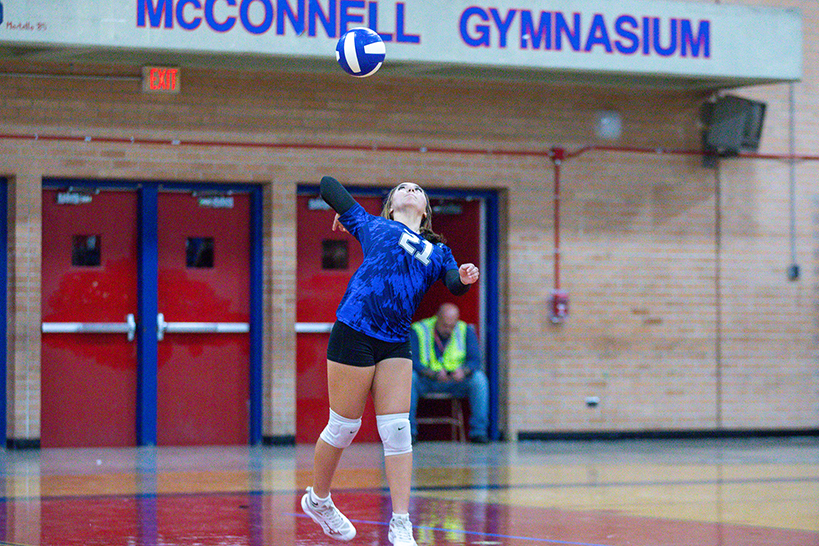 A girl in a tie-dye blue jersey spikes the volleyball