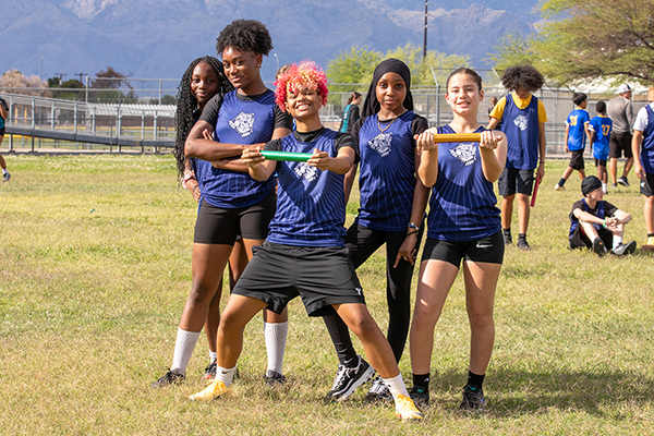 Members of the track team hold up batons on the field
