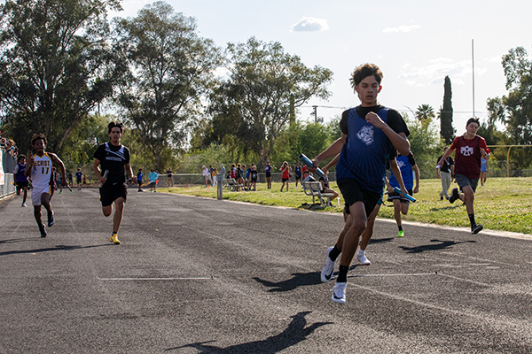 Boys run on the track holding batons during the relay race