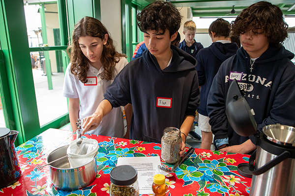 A boy pours tea leaves into a strainer over a pot