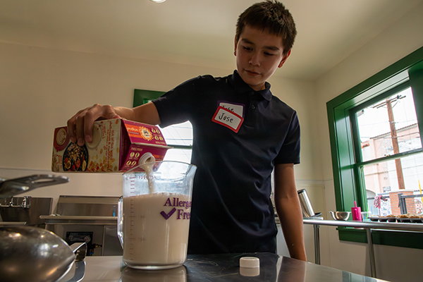A teen boy pours non-dairy milk into a measuring cup