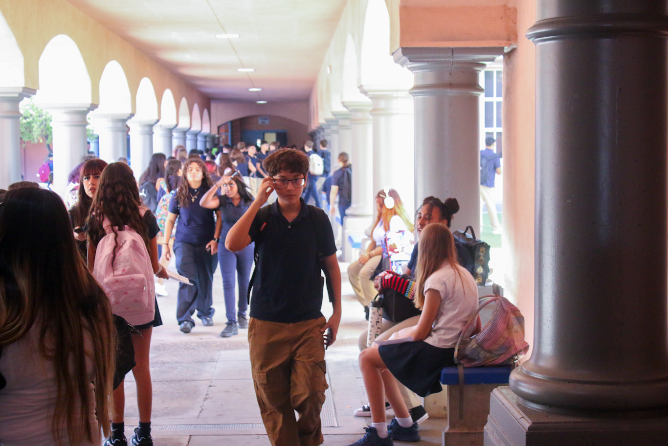 A preteen boy walks down the outside corridor between groups of students