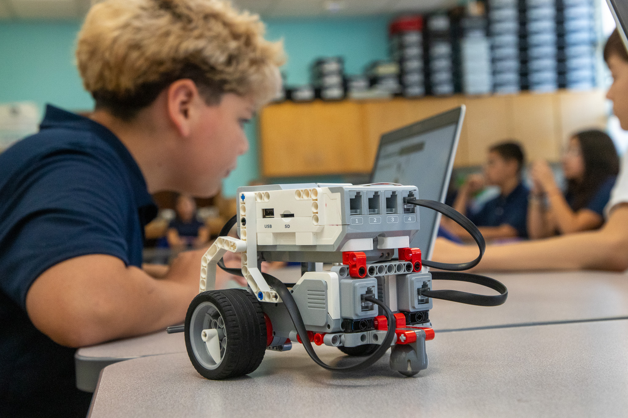 A preteen boy works on his laptop with a robot he built in front of him