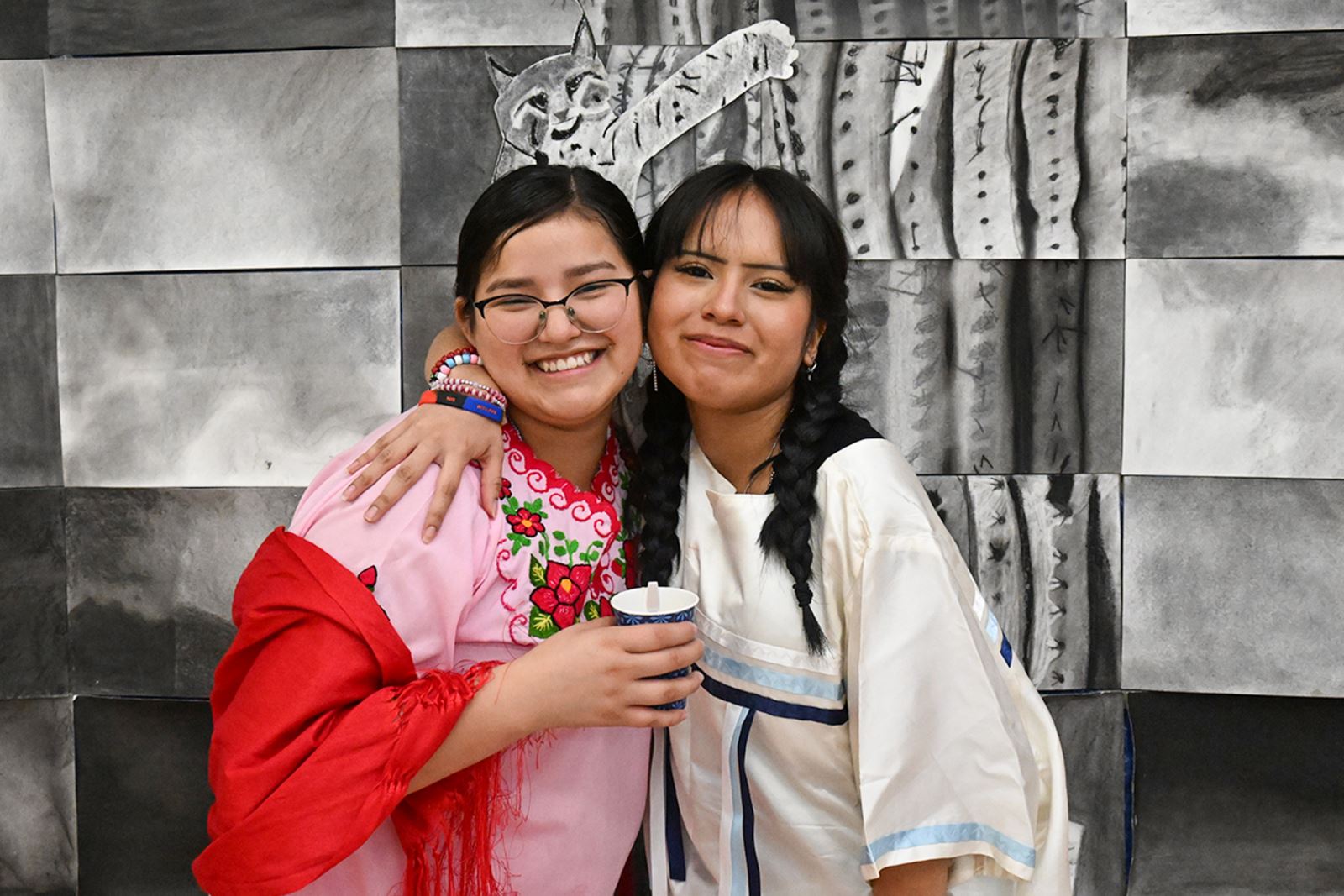 Two girls smile and pose in traditional Indigenous clothing.